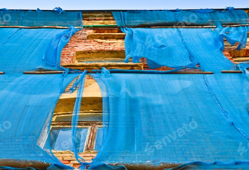 Preview: The facade of an old ruinous building is mantled with some blue curtains to protect the pedestrians