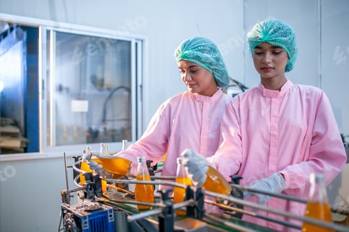 Preview: Asian woman worker is checking product bottles of fruit juice on the production line.