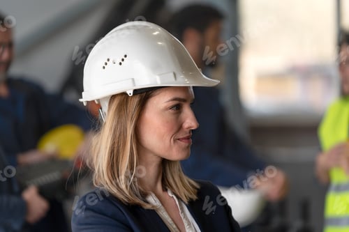 Preview: Side view of a female chief engineer in modern industrial factory looking at camera.