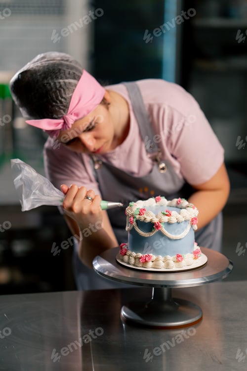 Preview: of a female baker in a professional kitchen decorating a blue cake with cream