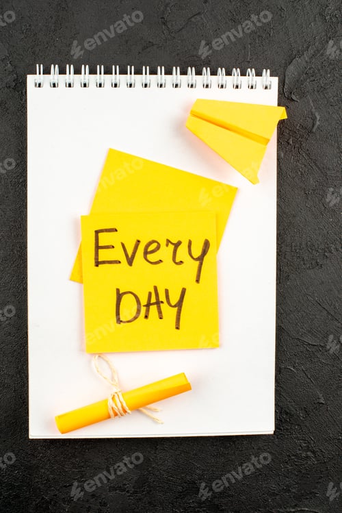 Preview: top view every day written on yellow sticky note scroll sticky note on spiral notepad on dark