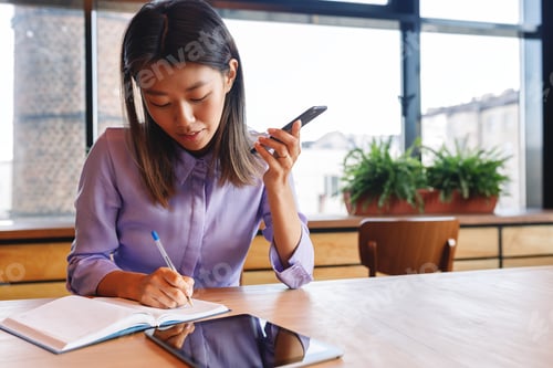 Preview: Young businesswoman using loudspeaker on mobile phone, working in cafe