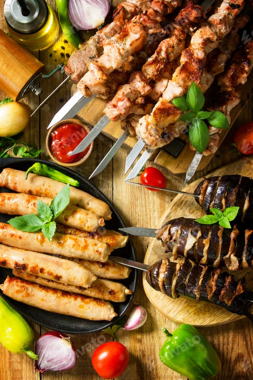 Preview: Grilled meat skewers, grilled sausages and grilled eggplant with bacon on rustic wooden table.