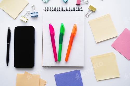 Preview: top view of smartphone with blank screen near notebook with colorful pens and stationery on white