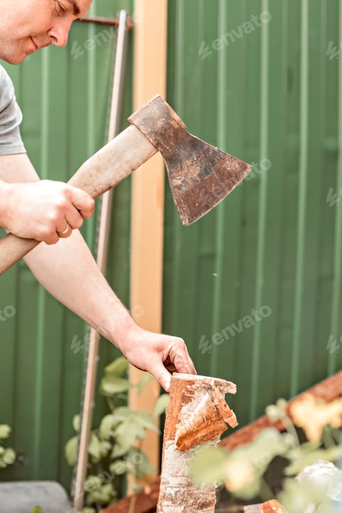 Preview: A young man is chopping wood with an axe in the backyard for a furnace. Life in a country house
