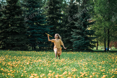 Preview: Caucasian child girl in a yellow dress in the park, runs with an airplane in her hands, active games