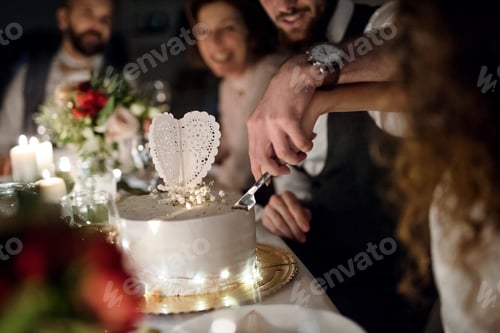 Preview: A midsection of young couple sitting at a table on a wedding, cutting a cake.