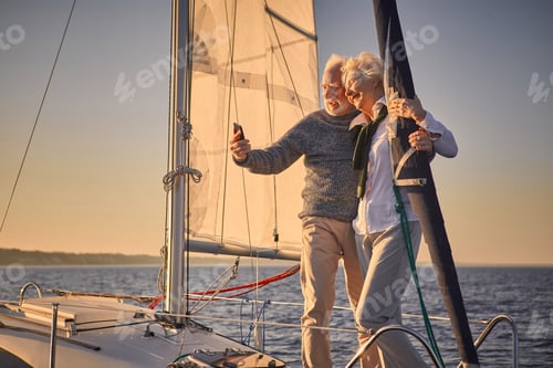 Preview: Beautiful senior couple hugging and smiling while making selfie on smartphone, they are standing on
