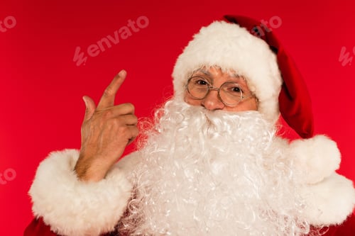 Preview: Portrait of bearded santa claus pointing with finger isolated on red