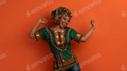 Preview: Joyful pretty black woman in african costume dancing on orange