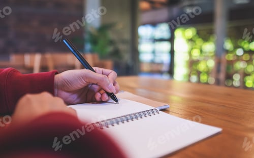 Preview: Closeup image of a woman writing on a notebook on the table