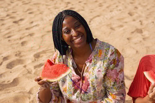 Preview: Happy young african woman eating fresh watermelon on the beach