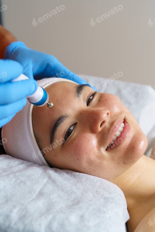 Preview: Professional beautician applying advanced facial treatment, rejuvenating smiling client