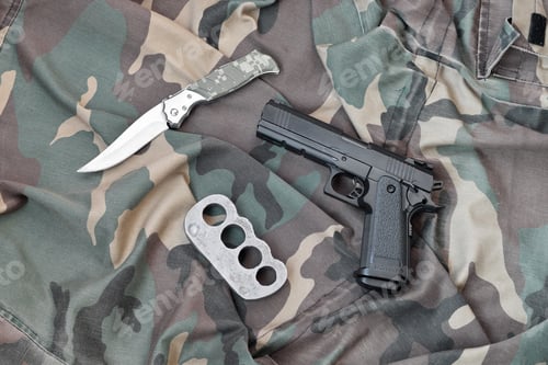 Preview: Handgun lies with brass knuckles and knife on camouflage militar