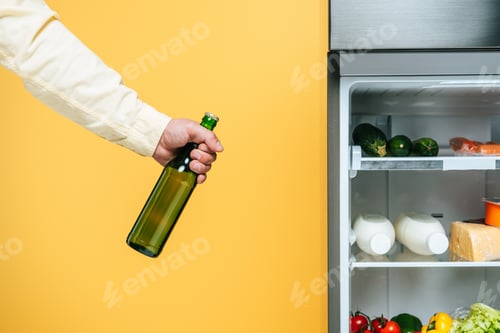 Preview: cropped view of man holding yogurt near open fridge with fresh food on shelves isolated on yellow