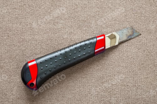 Preview: Close-up of isolated stationery retractable metallic knife with sharp blade on light cloth