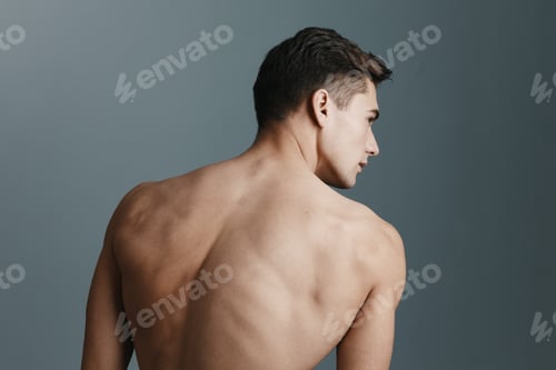 Preview: Sexy man with a naked back looks to the side on a gray background rear view of a fitness