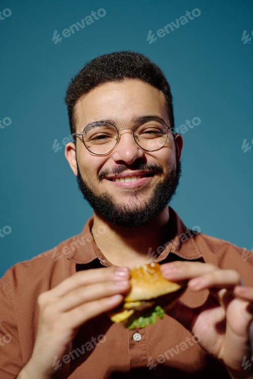 Preview: Portrait of Smiling Man Holding Burger against Blue Background