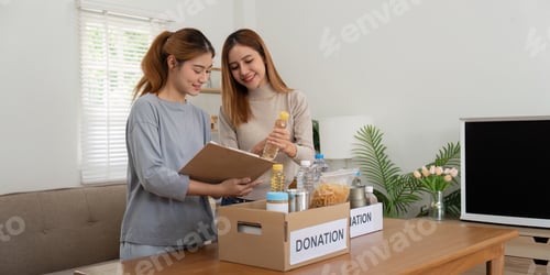 Preview: Donation and two woman volunteer asian of happy packing food in box at home. Charity