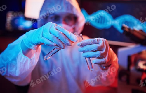 Preview: Nurse in mask and white uniform, holding tube with liquid and sitting in neon lighted laboratory