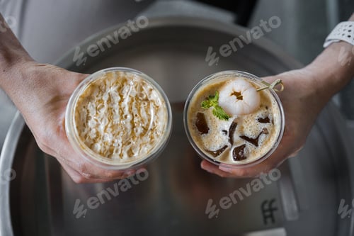 Preview: Hands of teenage girls holding glass of ice coffee together at cafe form above.
