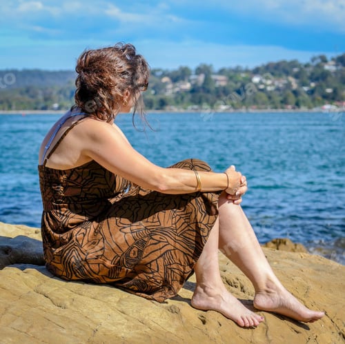 Preview: a woman in an brown dress sitting on the edge of a cliff