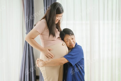 Preview: An Asian husband sits on sofa, gently holding his pregnant wife's stomach. He lovingly cares for
