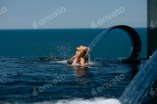 Preview: Young woman relaxing under swimming pool waterfall jet