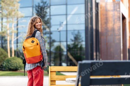 Preview: Cheerful young blonde hipster woman student with backpack looking back to camera.