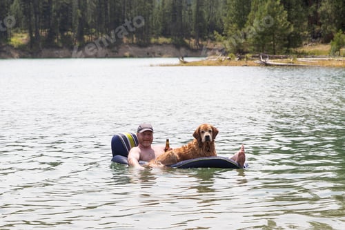 Preview: Happy man drinking a beer and floating on a lake with his golden retriever dog
