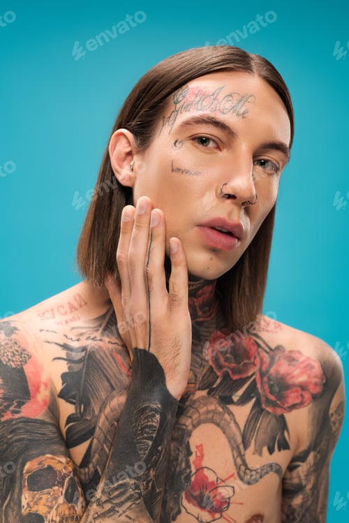 Preview: shirtless young man with tattoos looking at camera while touching smooth skin isolated on blue