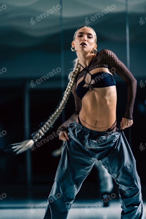 Preview: Sexy young blonde with a long braid ponytail posing in the studio in stylish outfit