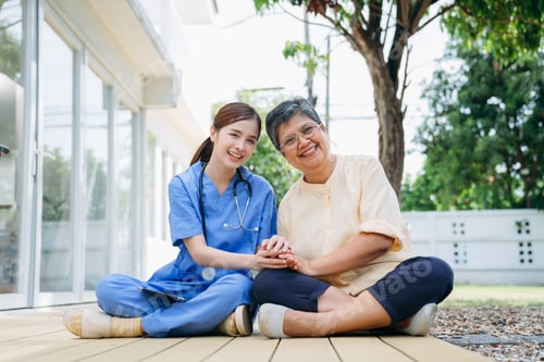 Preview: Nurse in a blue uniform is sitting on the ground with a woman in a yellow shirt.