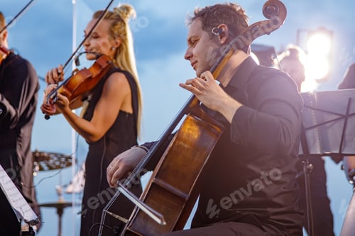 Preview: Male violoncellist playing in orchestra at outdoor concert