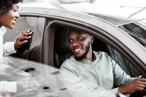 Visualização: Test drive. Homem negro sentado no banco do motorista de um carro novo, escolhendo o veículo com sua esposa e filha