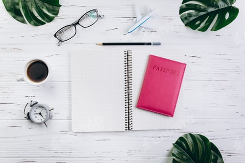 Preview: Wooden table with cup of coffee, alarm clock, passport, airplane, glasses, notebook and green.