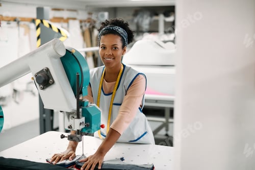 Preview: Happy black textile worker cutting fabric with a machine in clothing factory.