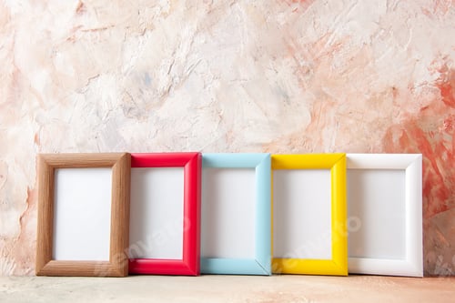 Preview: Front view of empty colorful photo frames leaning against the wall nude color wall with free space