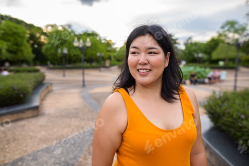 Preview: Beautiful overweight Asian woman thinking and smiling in park