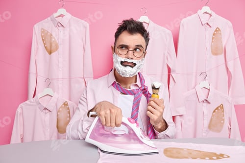 Preview: Serious man shaves and irons clothes at home concentrated away burned shirt as being deep in thougth