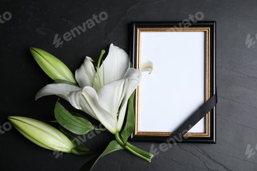 Preview: Funeral photo frame with ribbon and white lily on black table, flat lay. Space for design