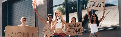 Preview: panoramic shot of five screaming multiethnic feminists holding smoke bomb, loudspeaker and placards