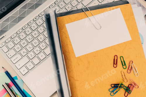 Preview: Top view closeup of a laptop, notebook, pens and pencils, paper clips on the white desk