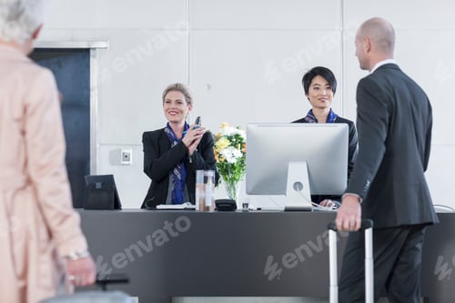 Preview: Two women behind reception desk in hotel lobby helping guests