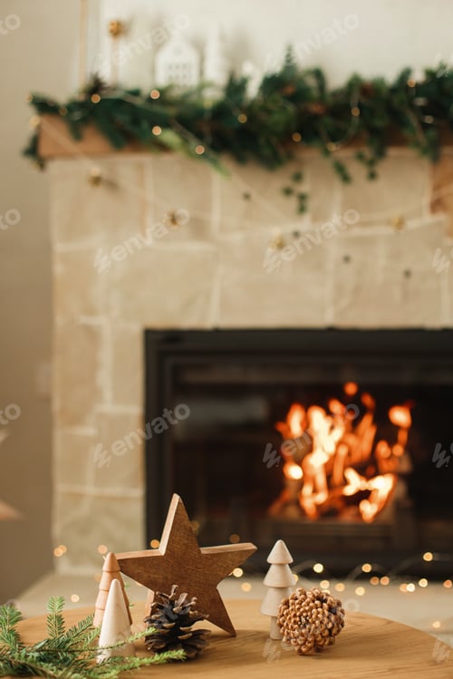 Preview: Stylish christmas wooden trees, candle, star, pine cones and fir branches on table against fireplace