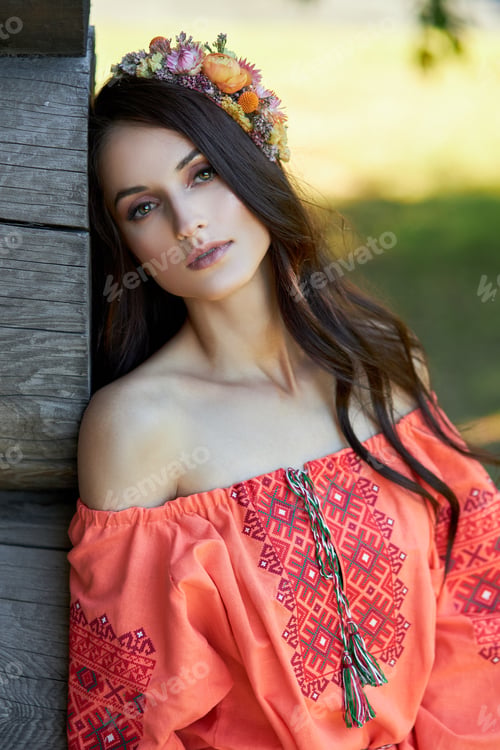 Preview: Beautiful Slavic woman in an orange ethnic dress and a wreath of flowers on her head. Beautiful