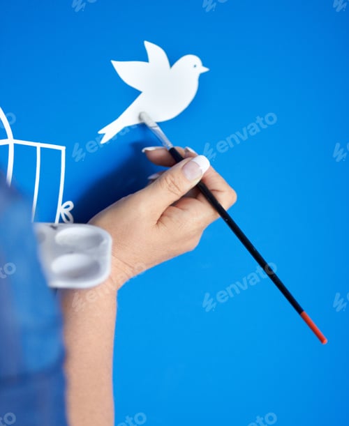 Preview: Creativity in flight. Closeup of a female artist painting a bird on a blue background.