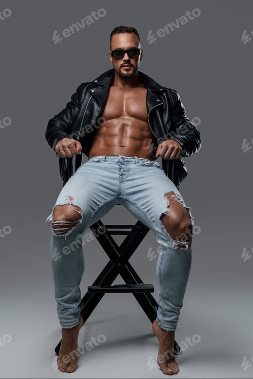 Preview: Handsome male model seated on a studio chair against grey backdrop