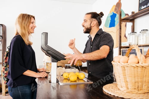 Preview: Customer Engaging in Friendly Conversation With Smiling Storekeeper at Grocery Checkout