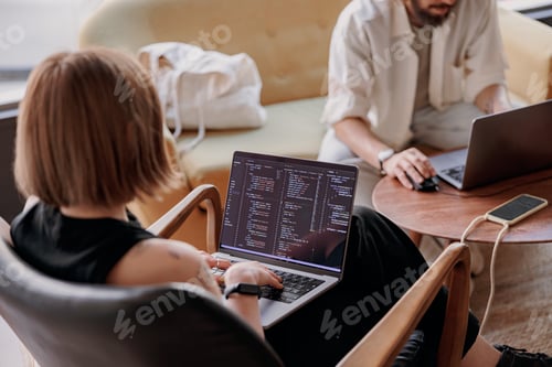 Preview: Back view of young woman programmer writes program code on laptop while sitting in modern coworking